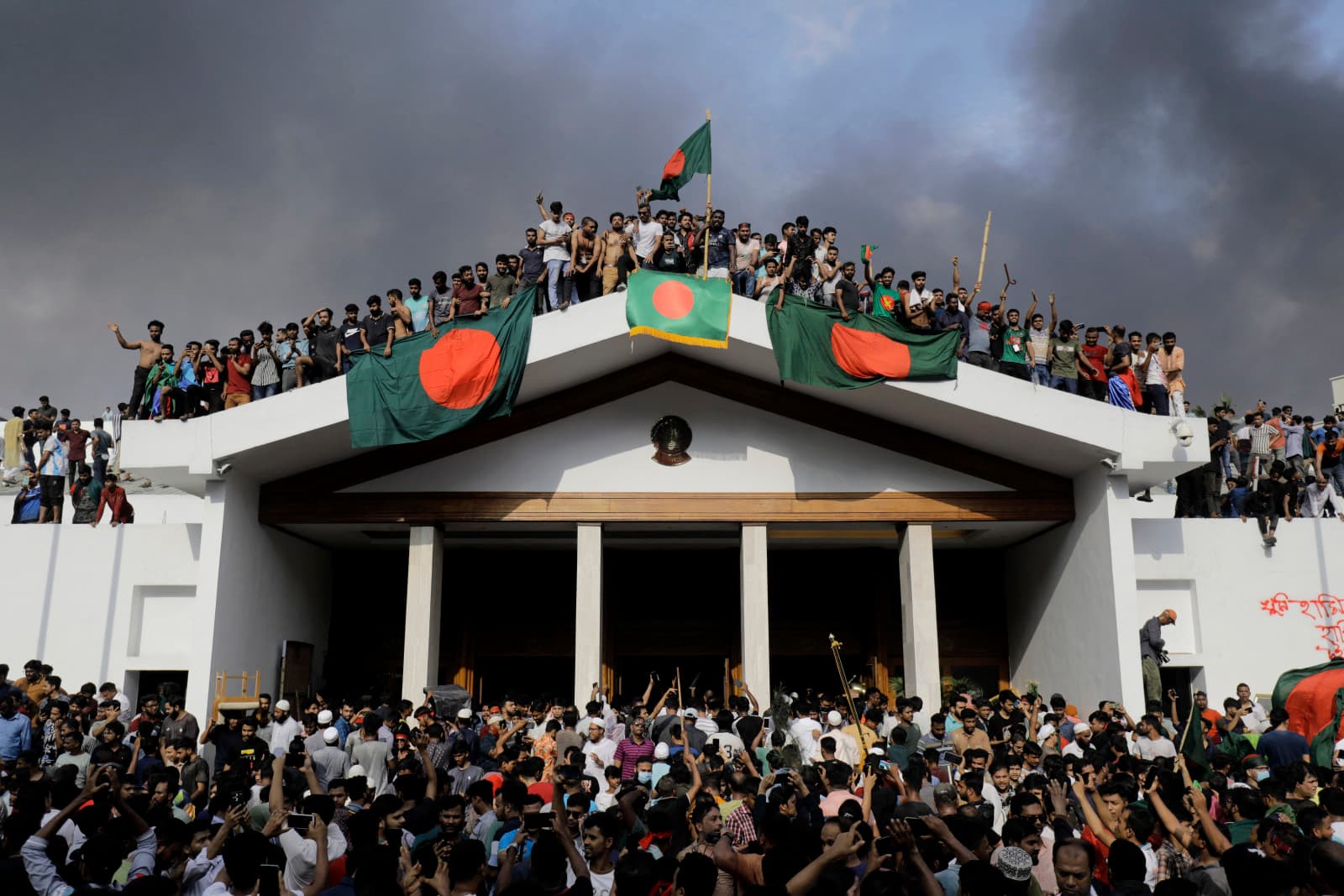 Anti-government protestors display Bangladesh’s national flag as they storm Prime Minister Sheikh Hasina’s palace in Dhaka on August 5, 2024 (K.M. ASAD/AFP via Getty Images)