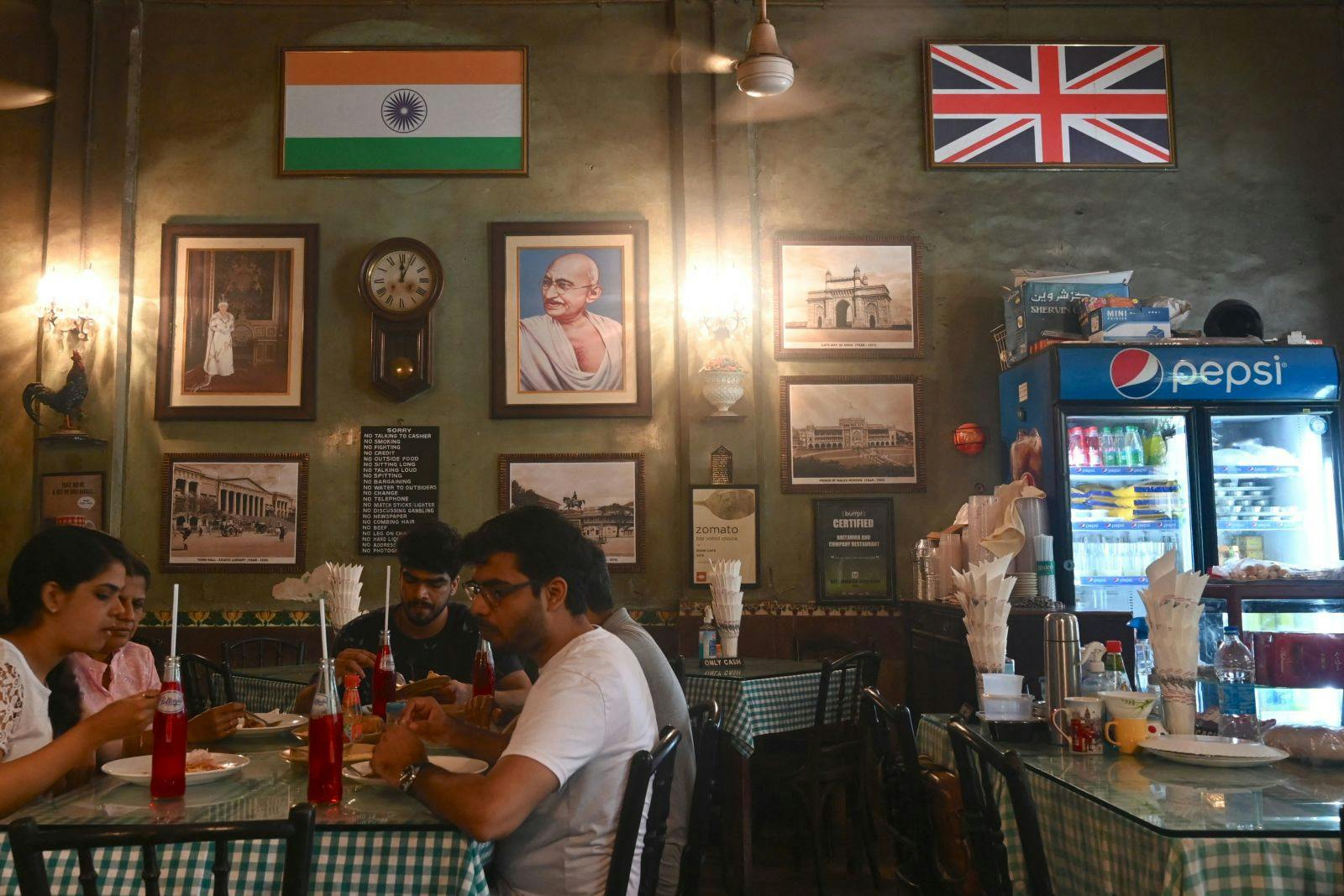 People eat lunch beside a portrait of Queen Elizabeth II alongside national flags of India and Britain, at a restaurant in Mumbai on September 9, 2022 (INDRANIL MUKHERJEE / AFP via Getty Images)