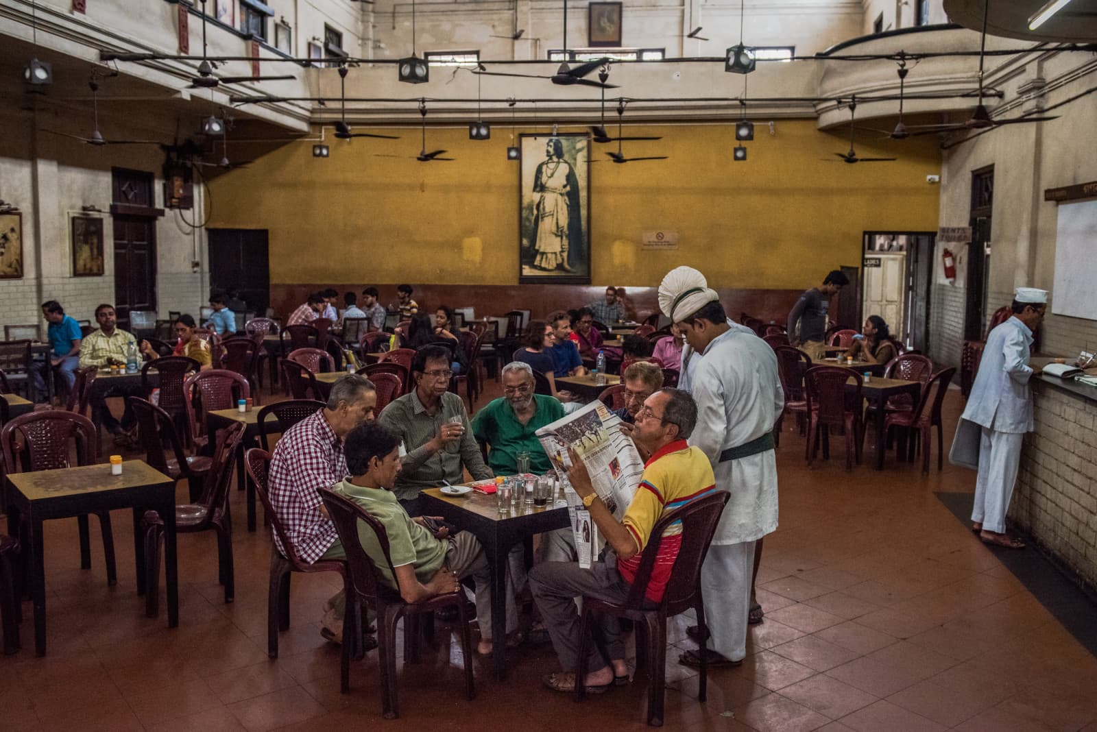 Indian customers are served inside the Indian Coffee House, established in 1942, on Bankim Chatterjee street in Kolkata. A portrait of Bengali writer, musician and artist Rabindranath Tagore hangs on the back wall. (REBECCA CONWAY/AFP via Getty Images)